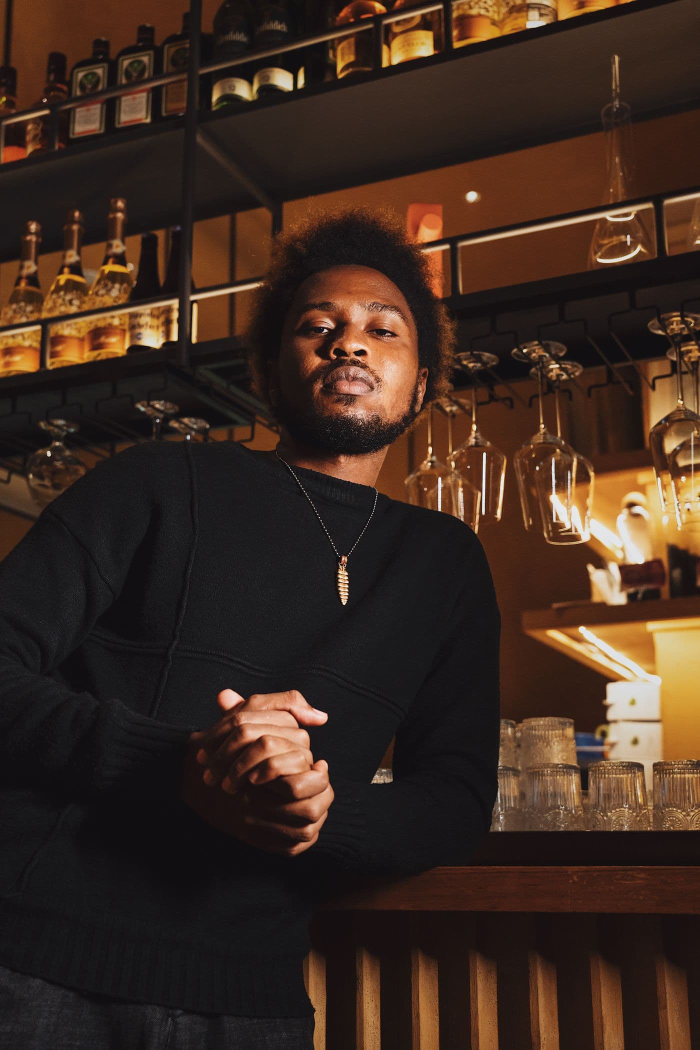 A man in a black sweater at a warmly lit cocktail bar