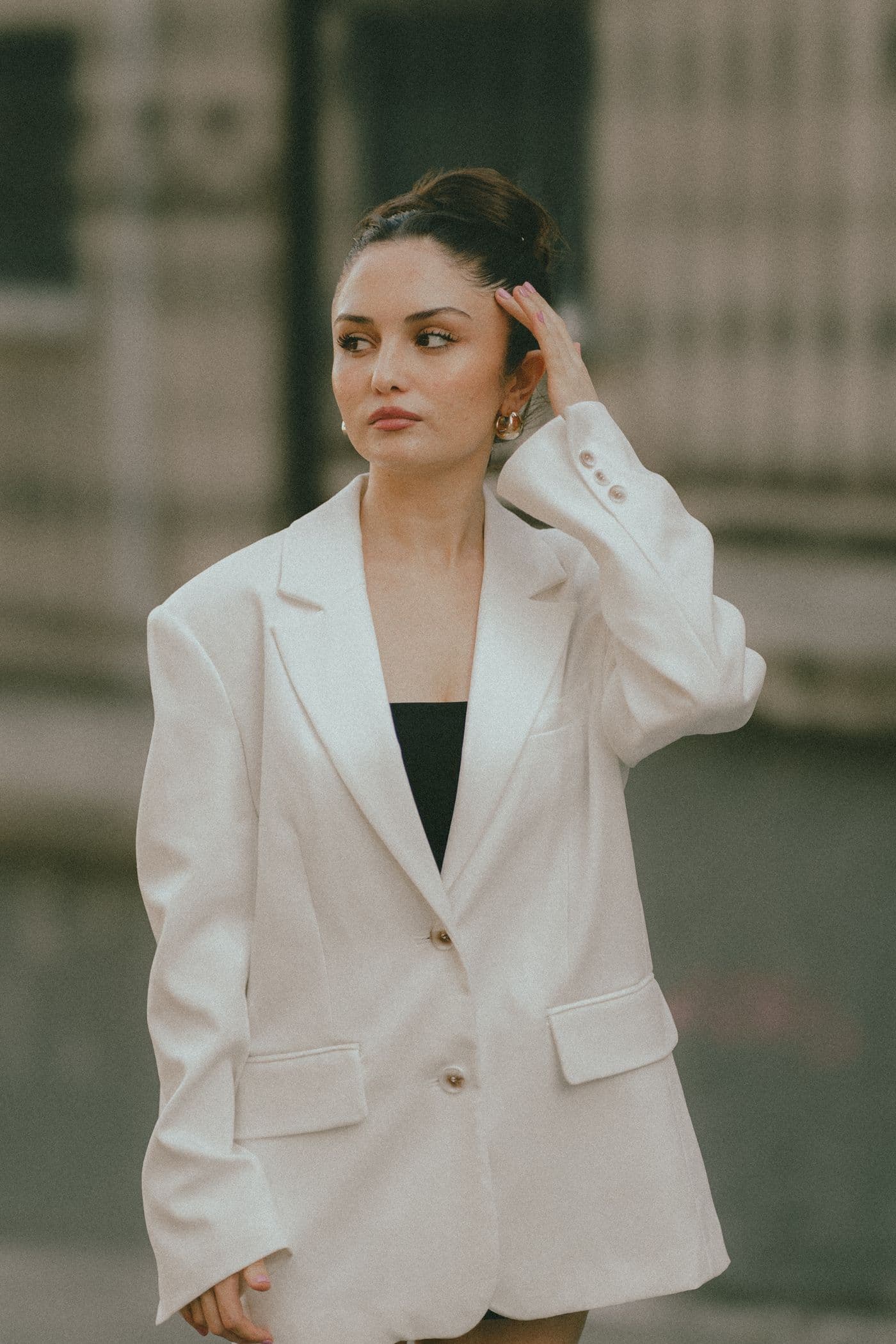A woman in a tailored ivory blazer, hand resting in her hair