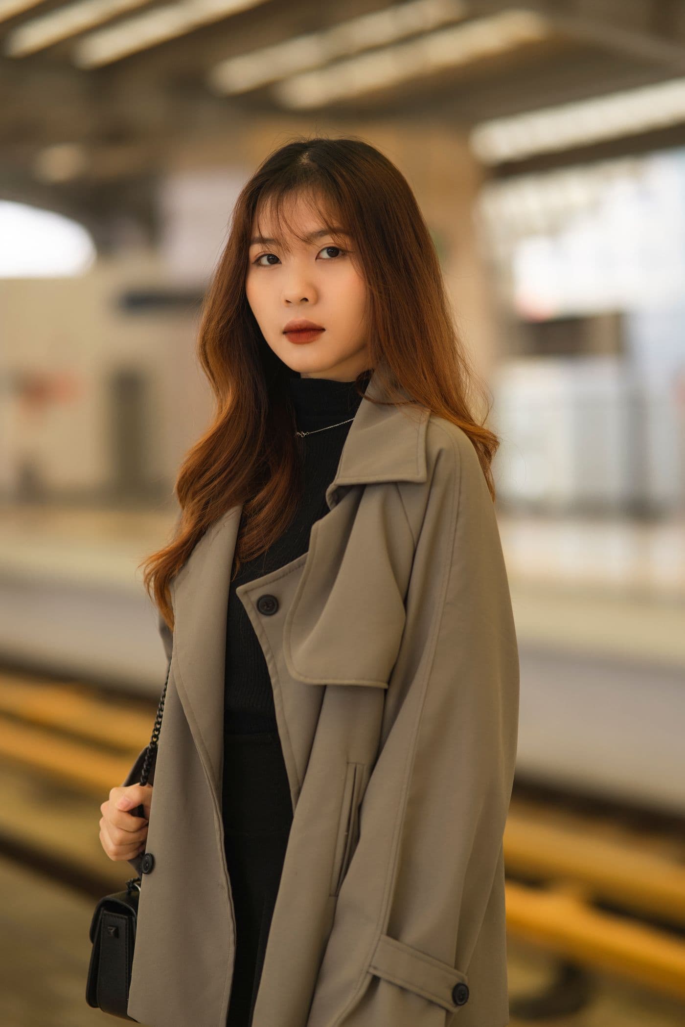 A woman in a camel trench coat on a warmly lit station platform